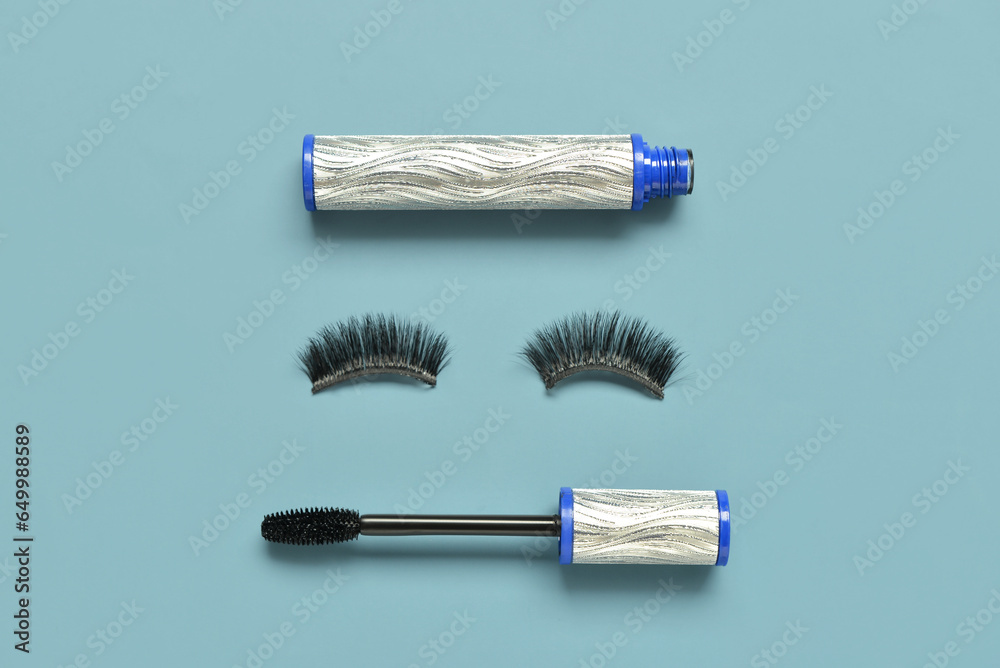 Black mascara in silver tube and fake eyelashes on blue background