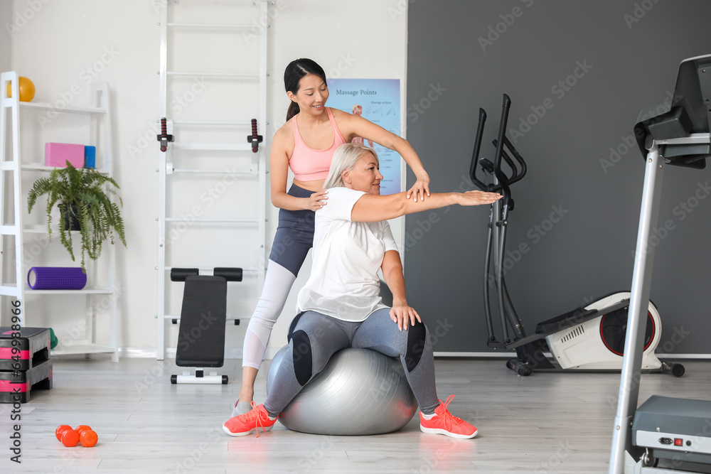 Mature woman training with therapist on fitball in rehabilitation center