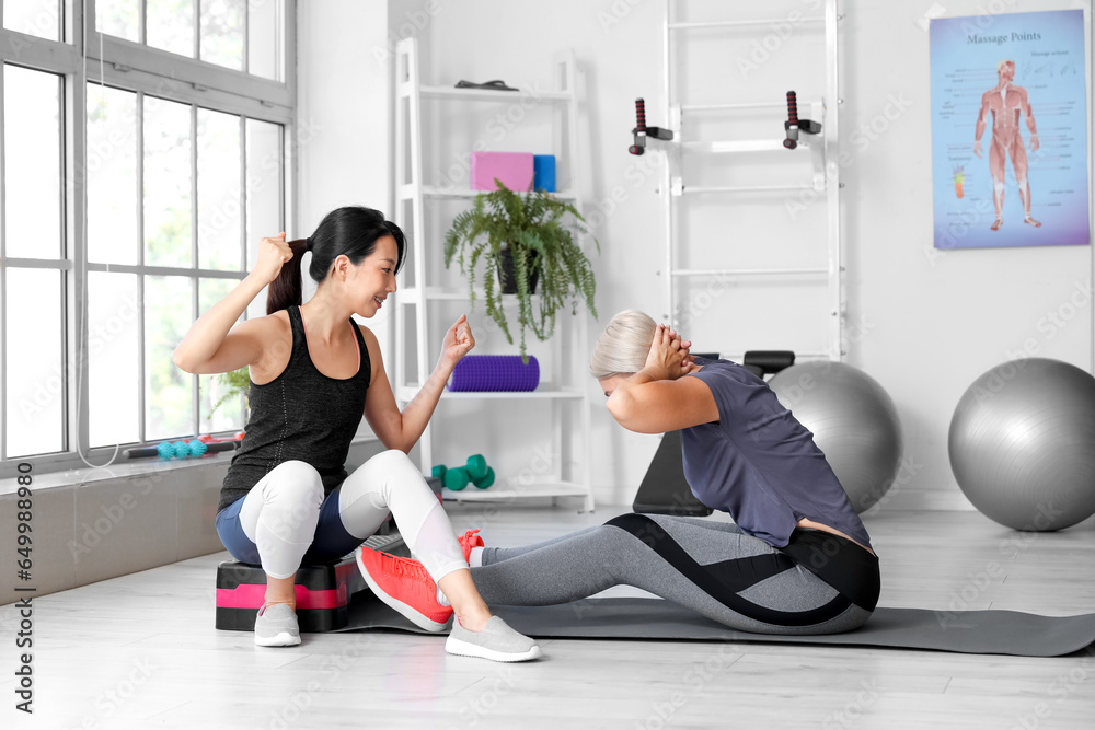 Mature woman training with therapist on mat in rehabilitation center