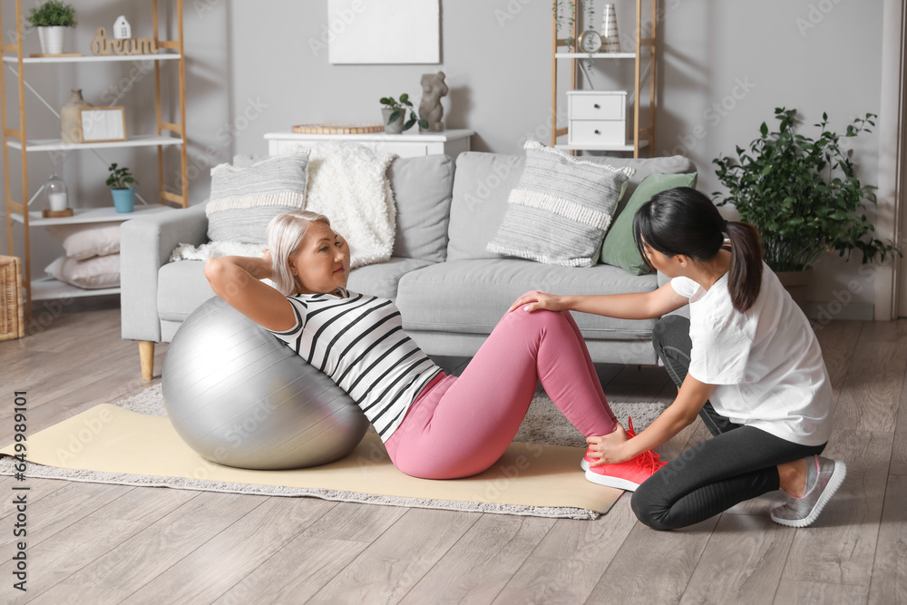 Mature woman training on mat with fitball and rehabilitation therapist at home