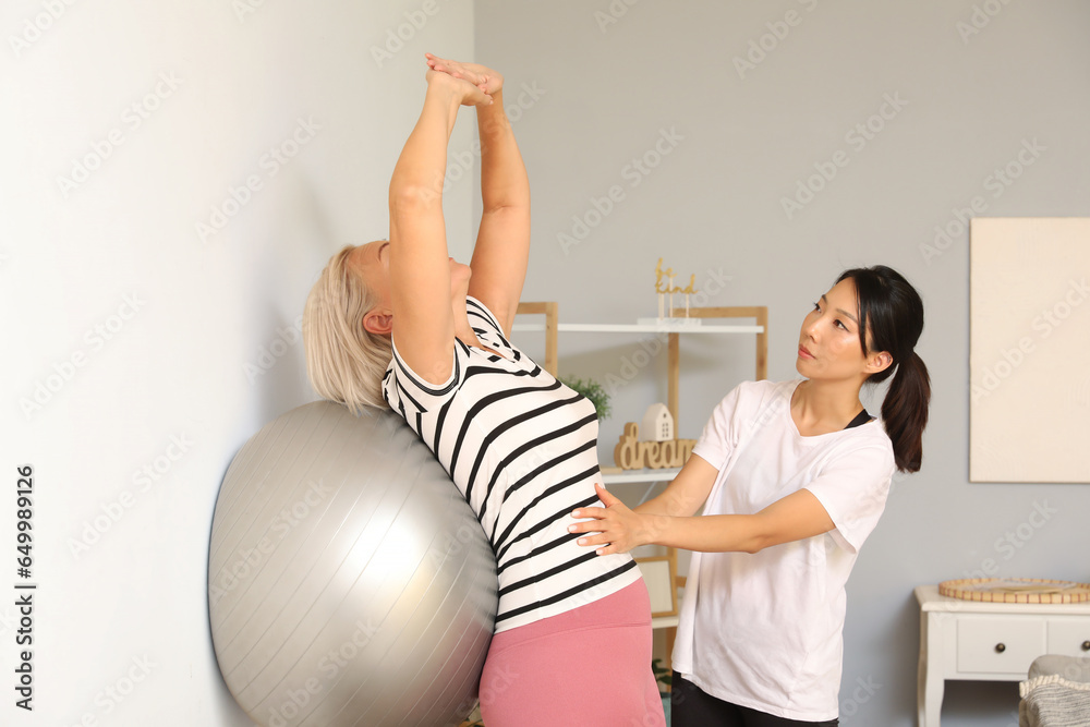 Mature woman training with fitball and rehabilitation therapist at home