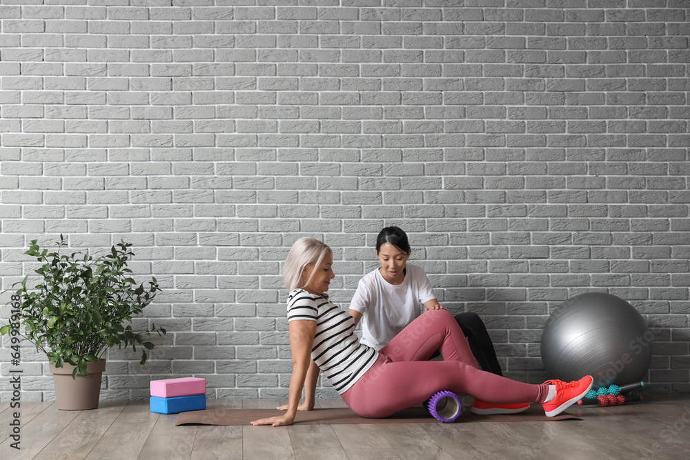 Mature woman training on mat with therapist in rehabilitation center