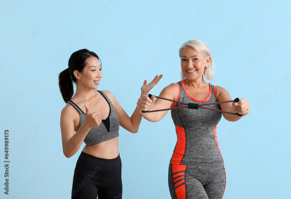 Mature woman training with expander and rehabilitation therapist on blue background