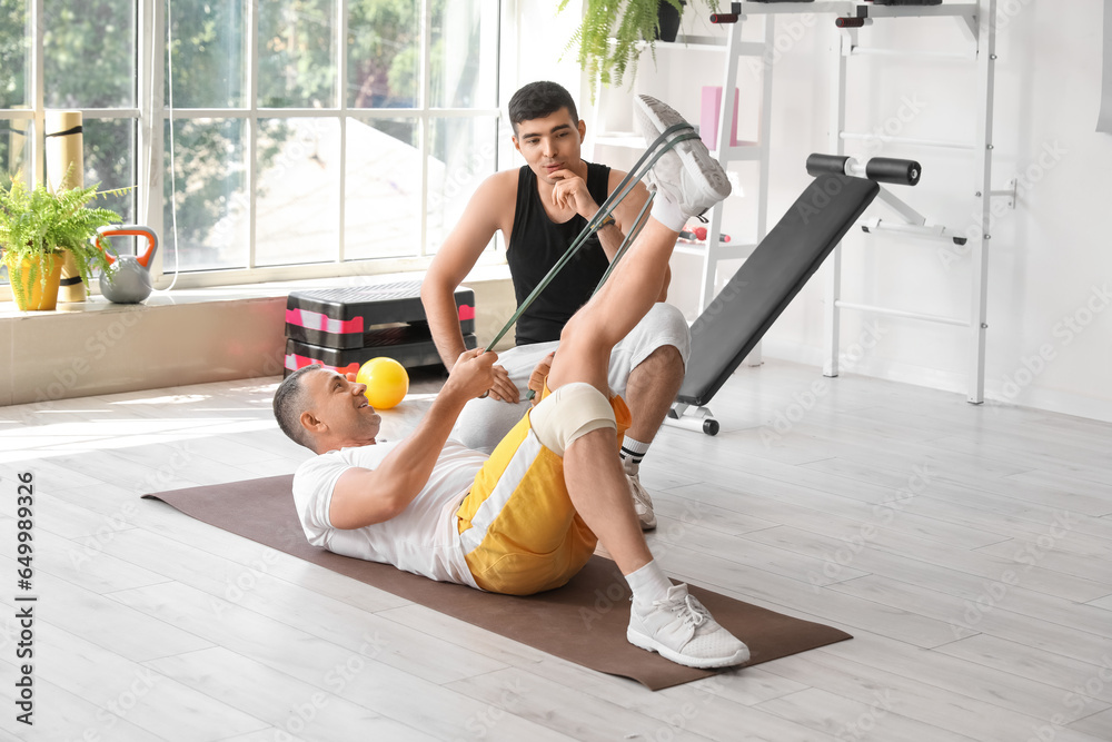 Mature man training with stretching tape and therapist in rehabilitation center