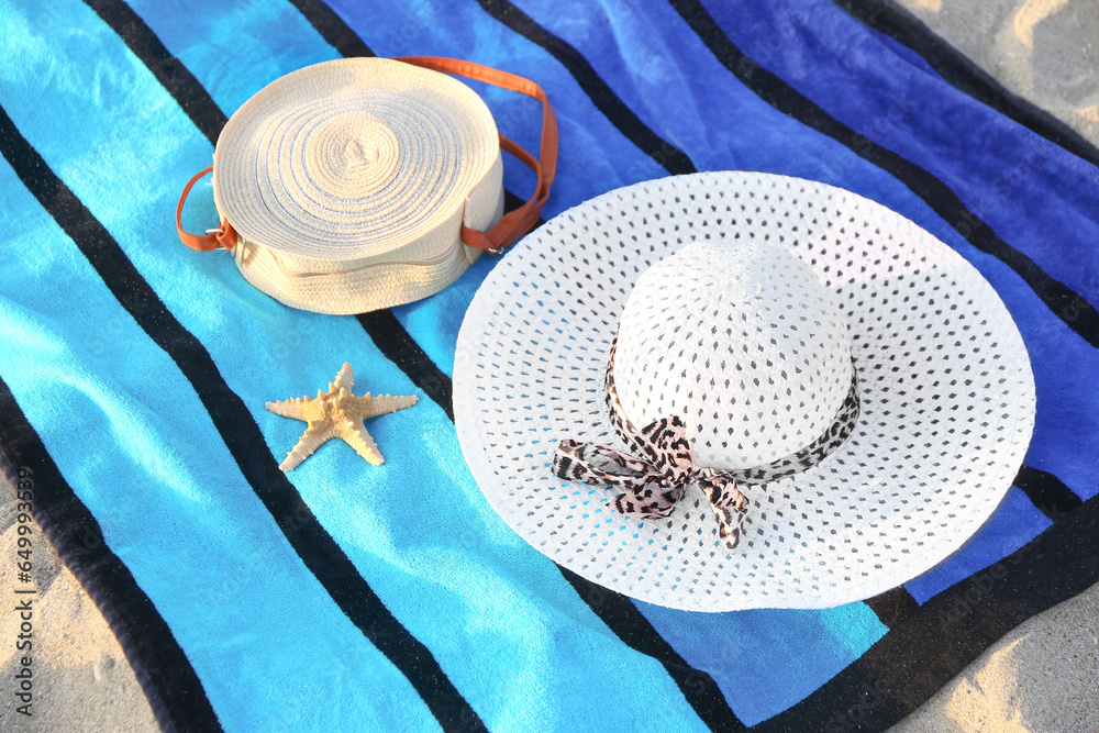 Colorful towel with stylish straw hat, bag and starfish on sand