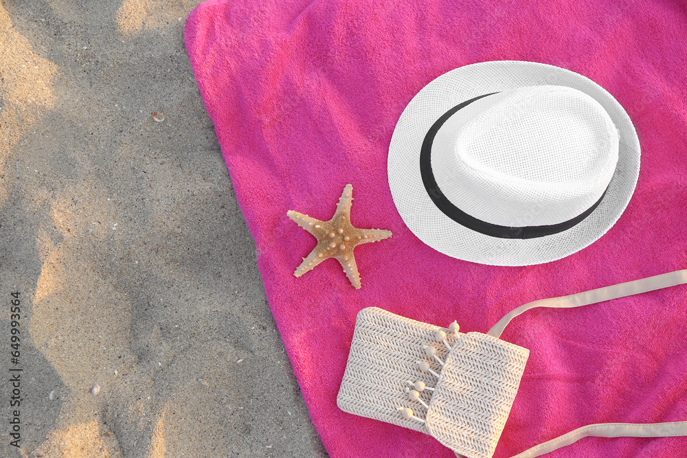 Towel with straw hat, bag and starfish on sand