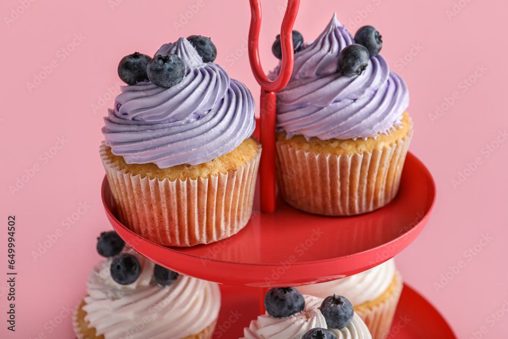 Dessert stand of tasty cupcakes with blueberries on pink background