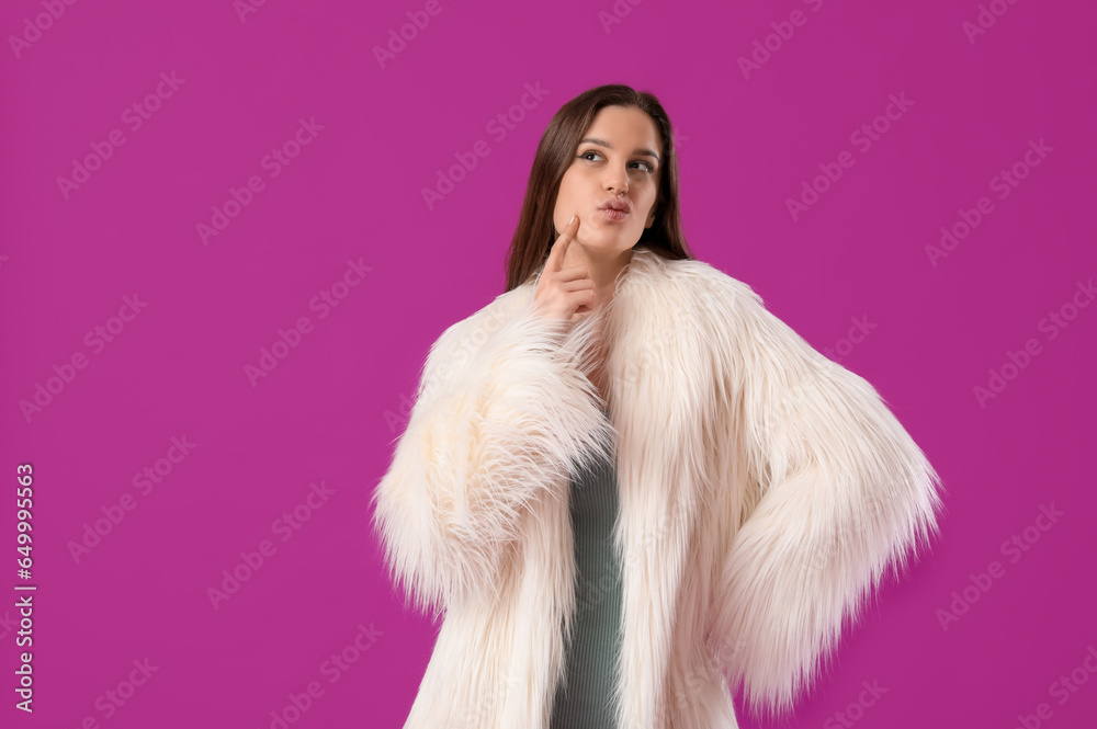 Thoughtful young woman in fur coat on purple background