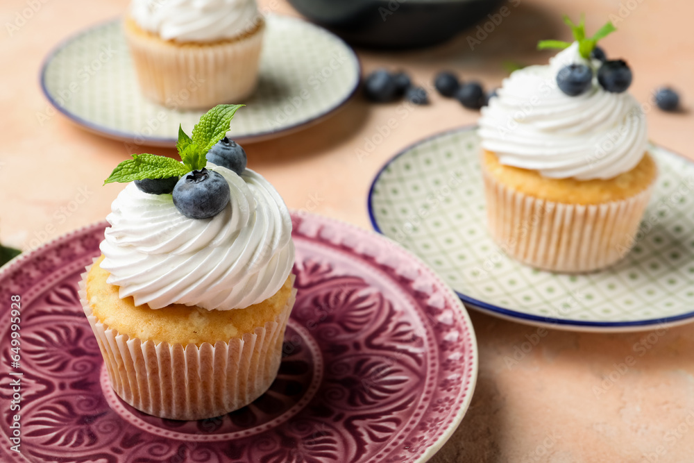 Plates of delicious cupcakes with blueberries and mint on pink background