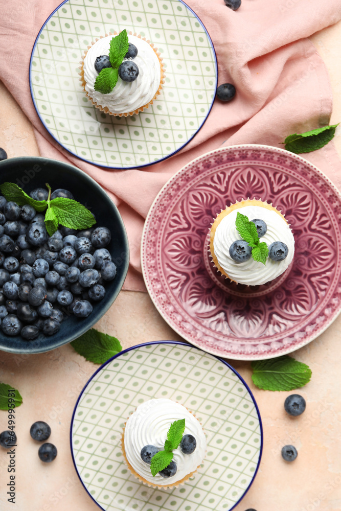 Plates of delicious cupcakes with blueberries and mint on pink background