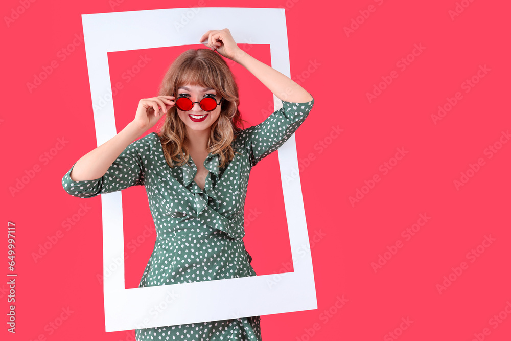 Young woman in sunglasses with frame on red background