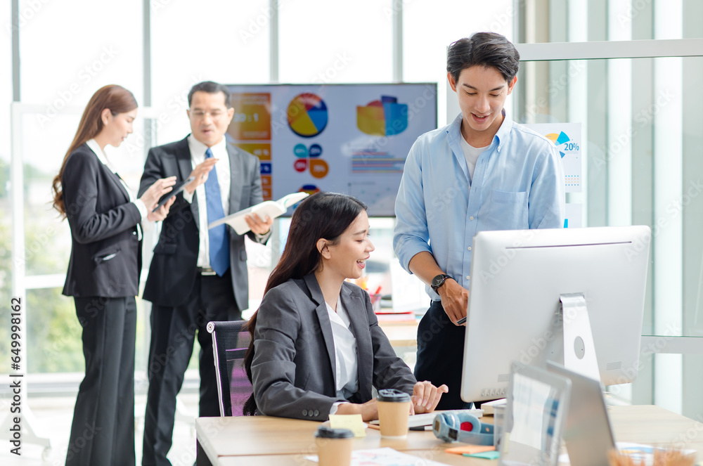 Asian professional successful male businessman mentor supervisor in casual outfit standing smiling teaching helping female businesswoman intern colleague in formal suit working via computer in office