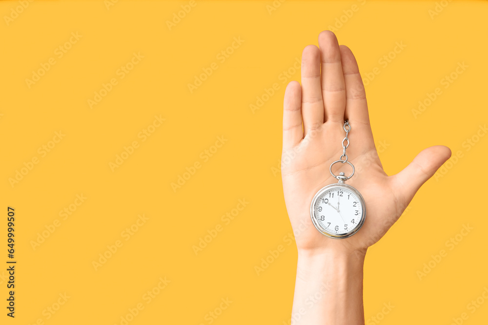 Female hand holding pocket watch on yellow background