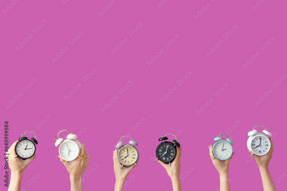 Hands holding different alarm clocks on purple background