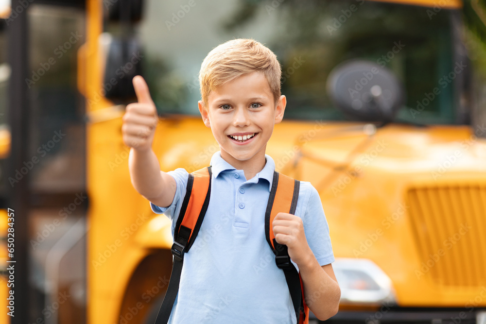 Happy Preteen Boy Showing Thumb Up While Standing Near School Bus Outdoors