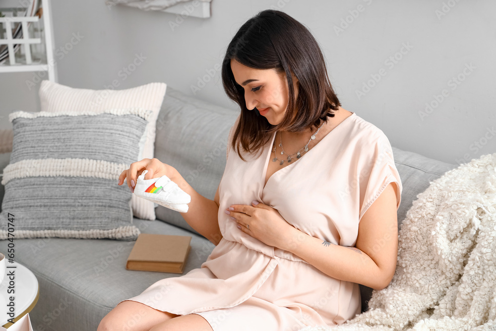 Young pregnant woman with baby booties sitting on sofa at home