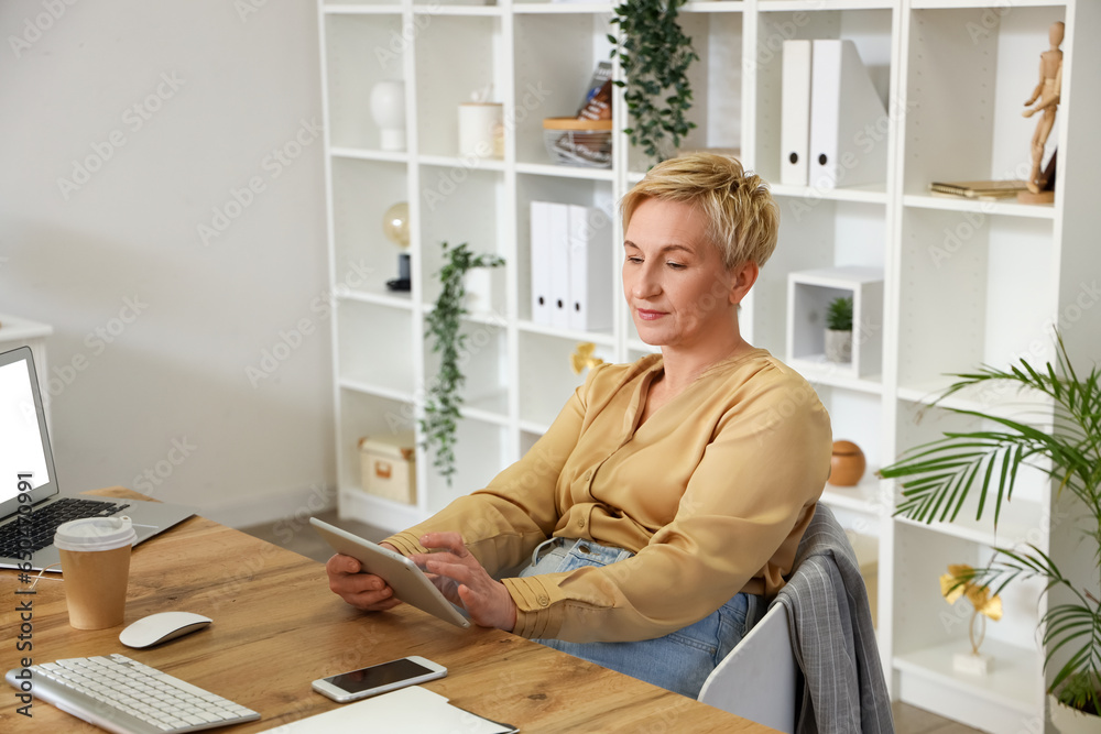 Mature female programmer working with tablet computer at table in office