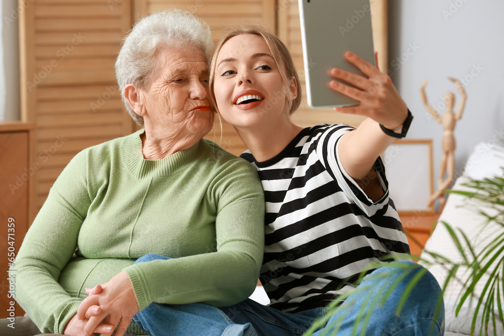 Young woman with her grandmother using tablet computer in bedroom