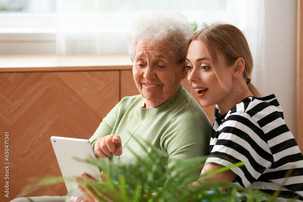 Young woman with her grandmother using tablet computer in bedroom