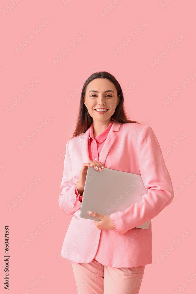 Young woman in stylish suit with laptop on pink background