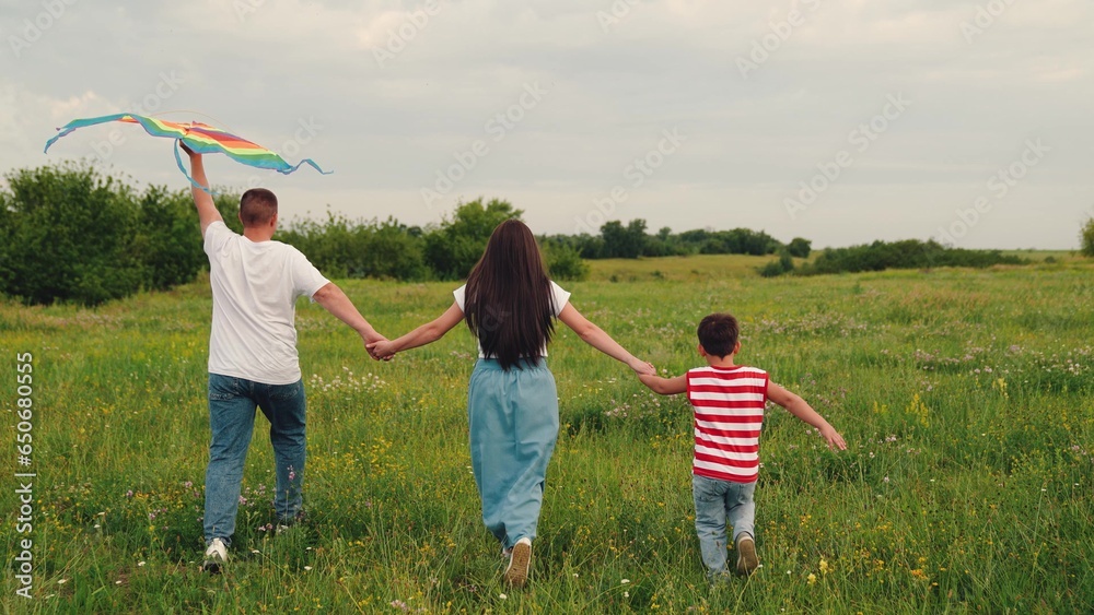 Young family is playing with kite in meadow. Happy family with kid boy in park playing with kite. Family walk on grass, child dreams of flying. Happy people together travel to nature. Kid wants to fly