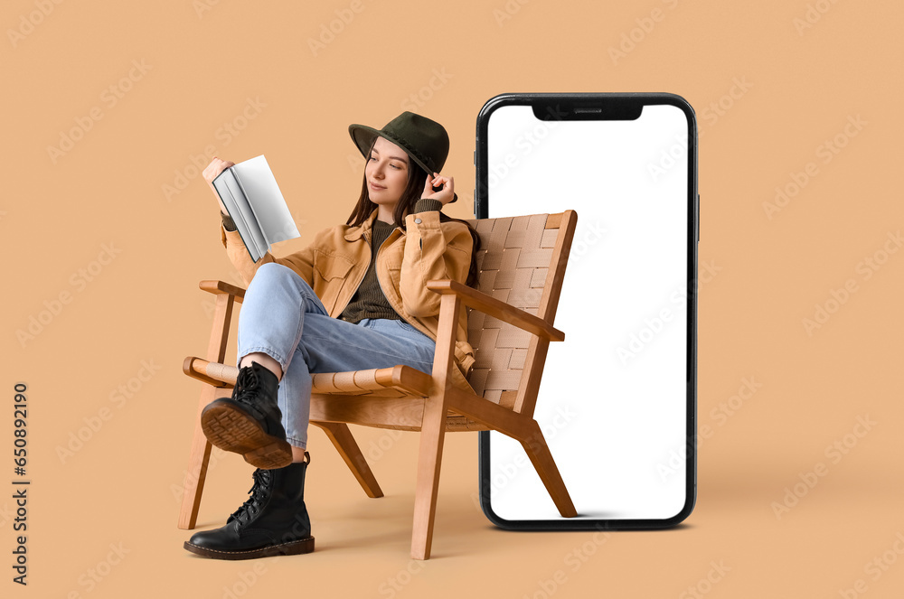 Young woman reading book in armchair on beige background