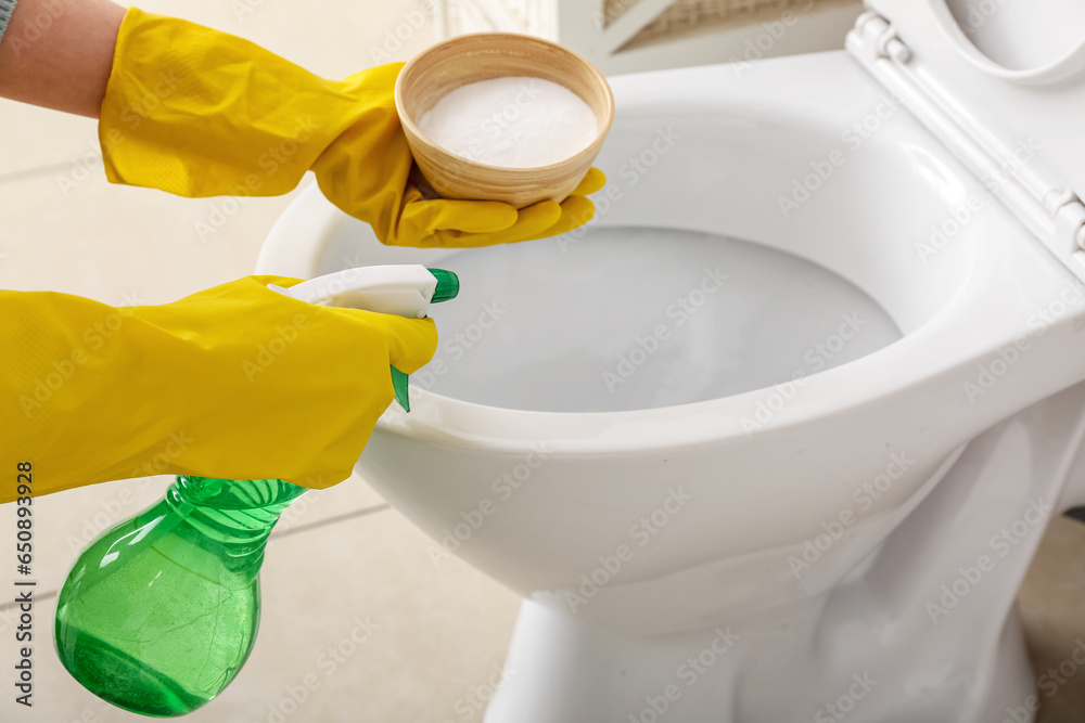 Woman in rubber gloves cleaning toilet bowl with baking soda and sprayer, closeup