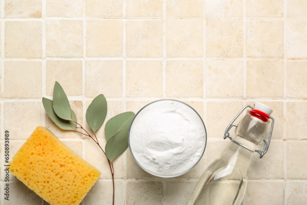 Bowl of baking soda, vinegar, cleaning sponge and eucalyptus branch on light tile background