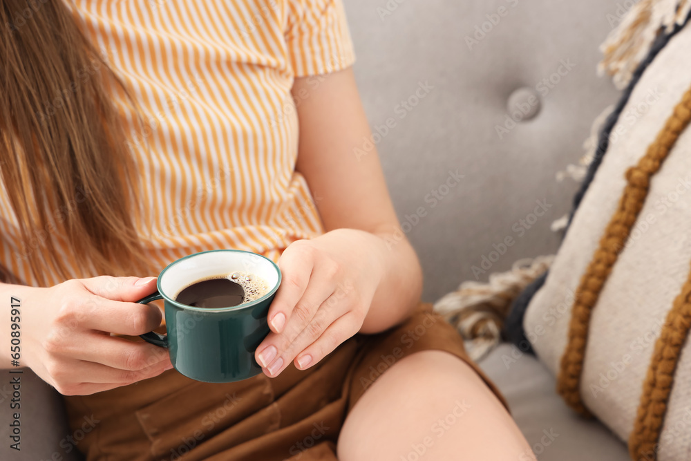 Woman sitting on cozy armchair and holding cup of delicious coffee