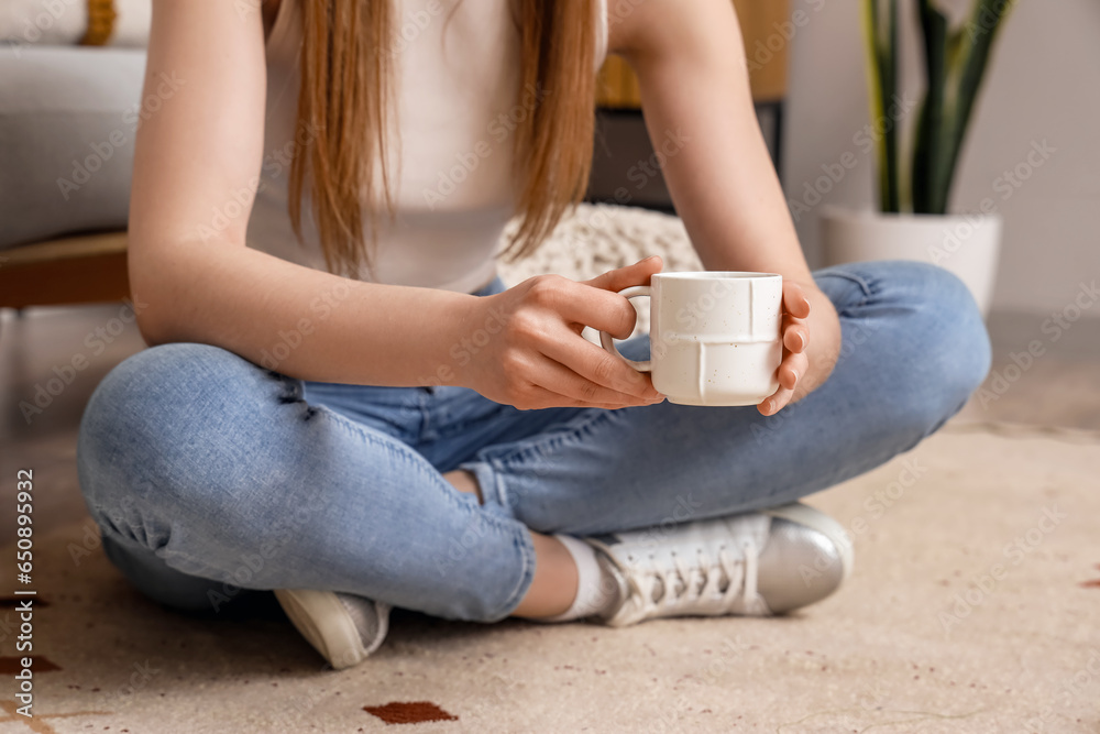 Woman sitting on floor and holding cup of delicious coffee