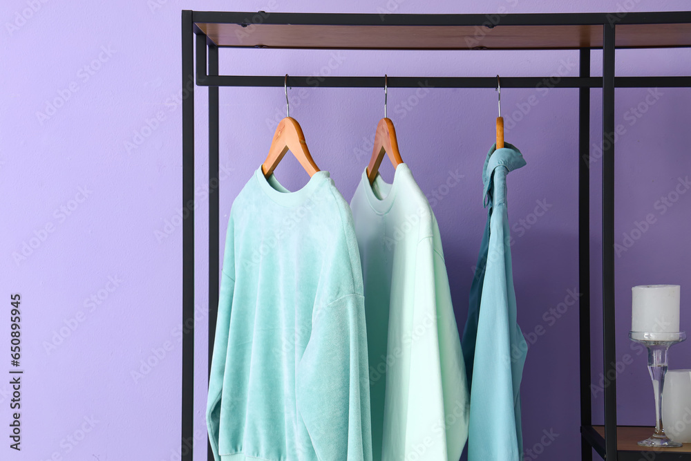 Stylish clothes hanging near lilac wall