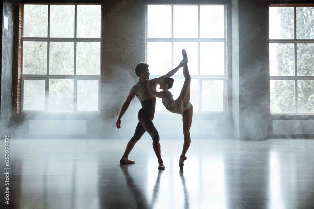 Man and woman ballet dancers performing together against studio background