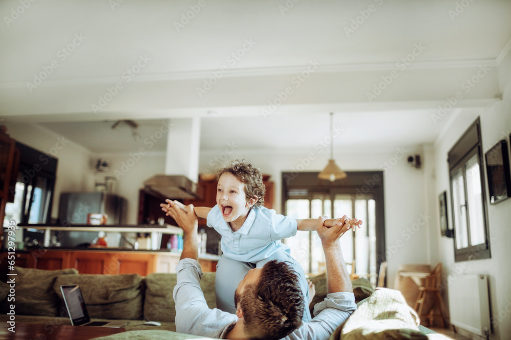 Happy young father and son playing together and having fun on the couch in the living room at home