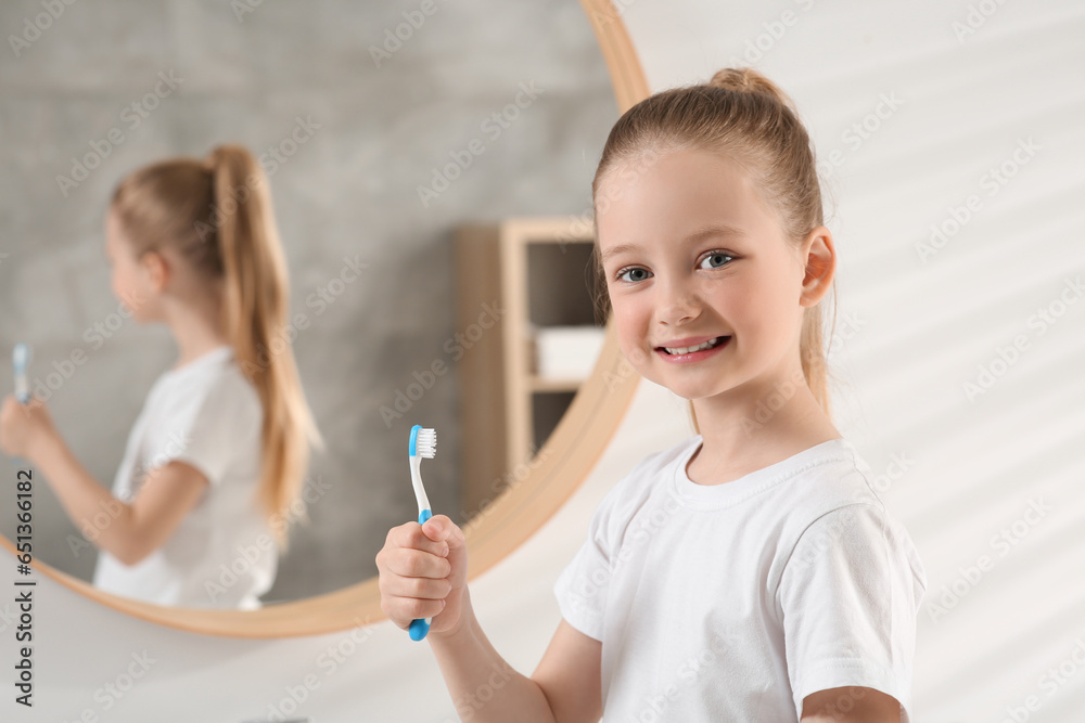 Cute little girl holding plastic toothbrush in bathroom, space for text