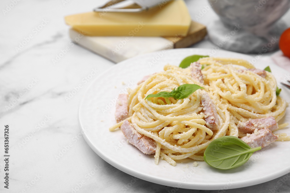 Plate of tasty pasta Carbonara with basil leaves on white marble table, closeup. Space for text