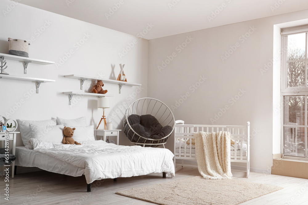 Interior of light bedroom with bed, baby crib and armchair