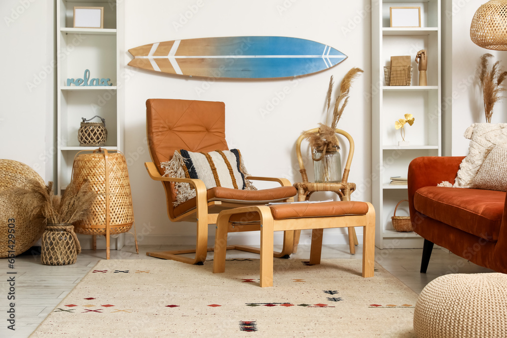 Interior of light living room with surfboard, brown sofa and armchair