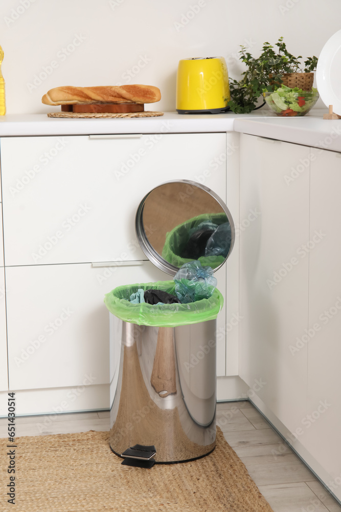 Opened trash bin with garbage in interior of light kitchen