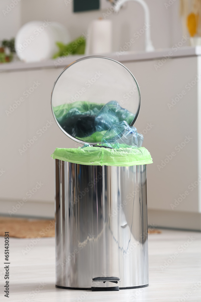 Opened trash bin with garbage in interior of light kitchen