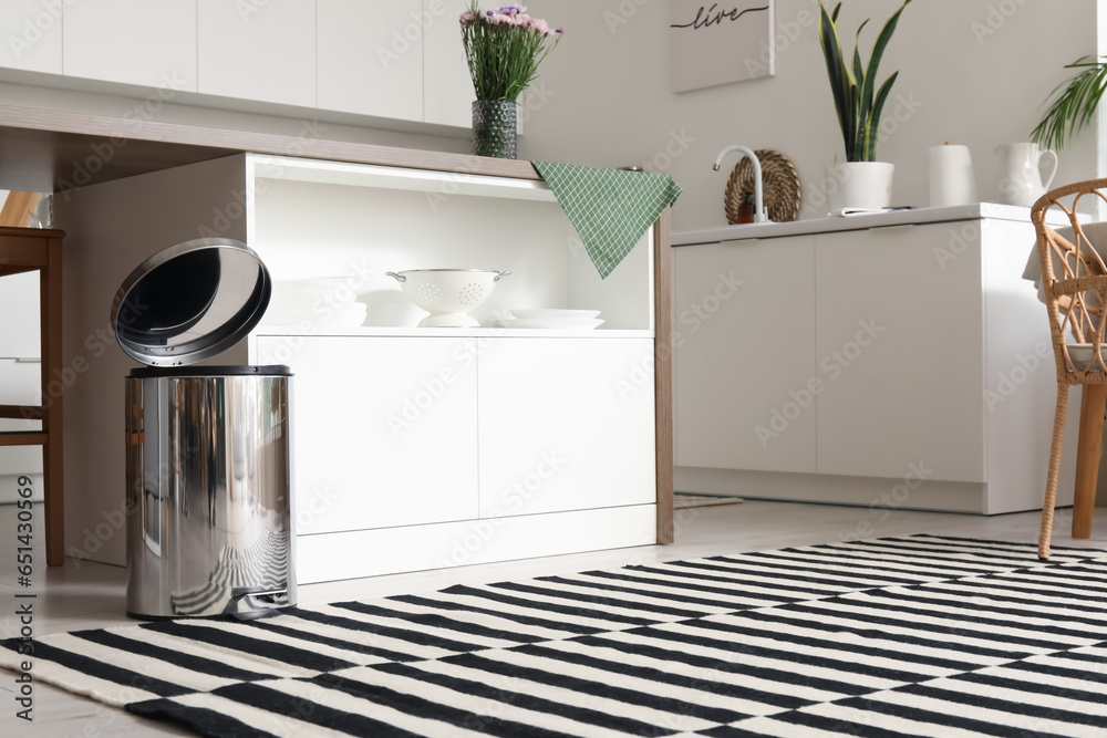 Opened metallic trash bin near table in interior of modern kitchen