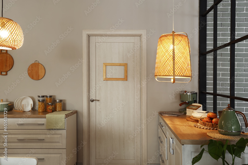 Interior of modern kitchen with glowing lamps, white counters and door at evening