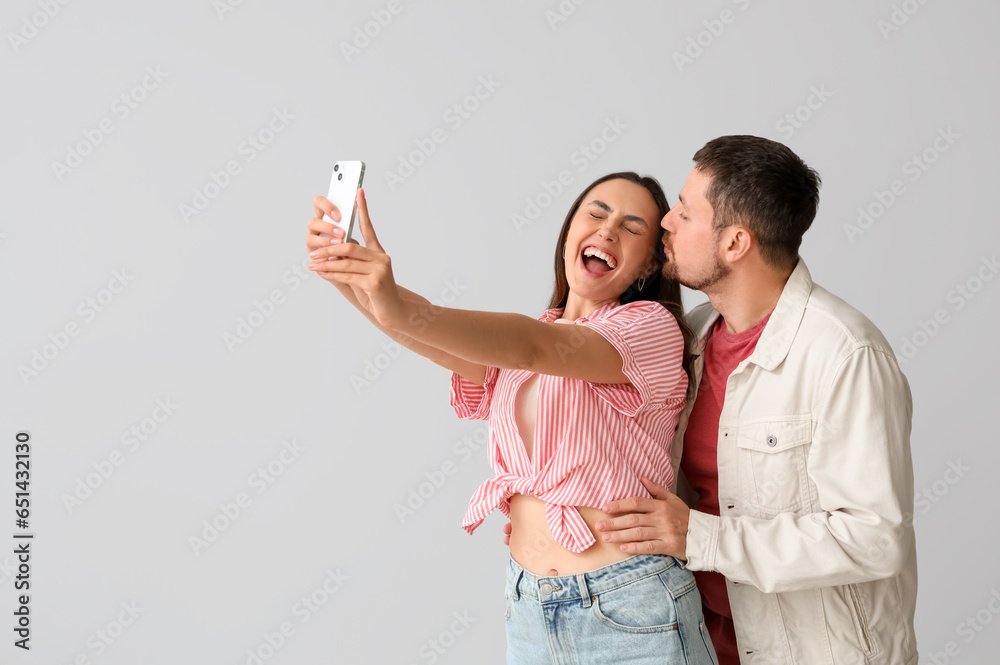 Happy young couple with mobile phone taking selfie on light background