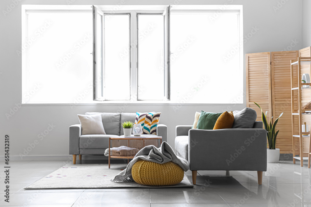 Cozy grey sofas and pouf with soft blanket in interior of light living room