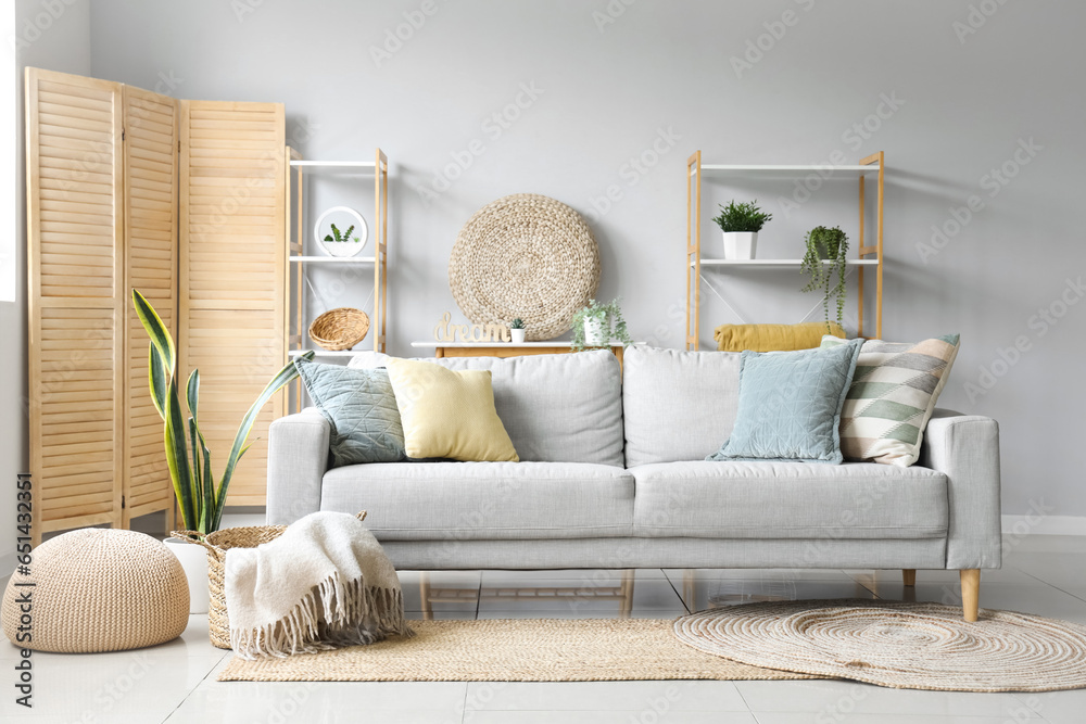 Cozy grey sofa and basket with soft blanket in interior of light living room