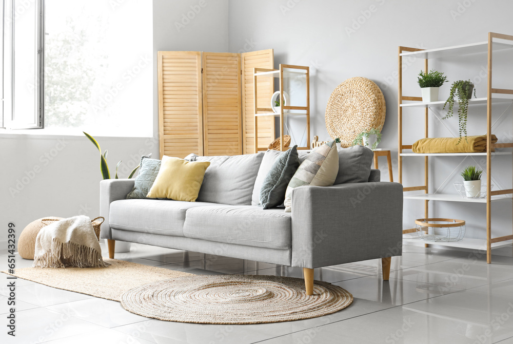 Cozy grey sofa and basket with soft blanket in interior of light living room