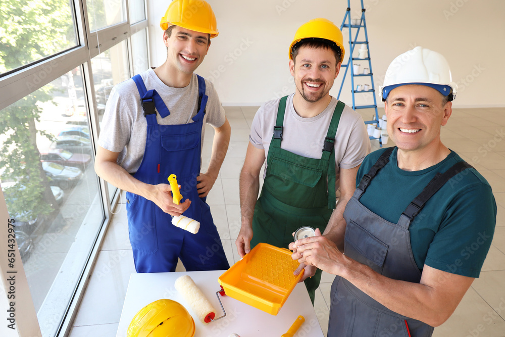 Team of male builders with paint rollers working in room