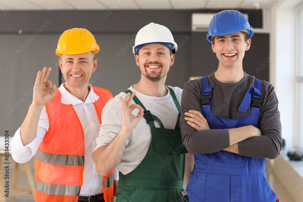 Team of male builders showing OK in room