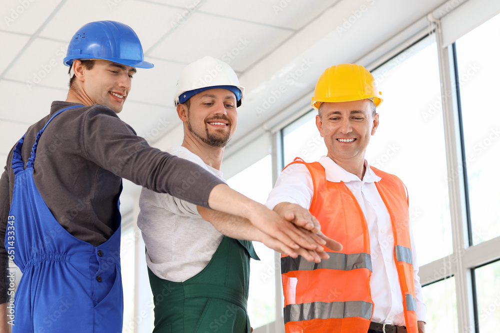 Team of male builders putting hands together in room