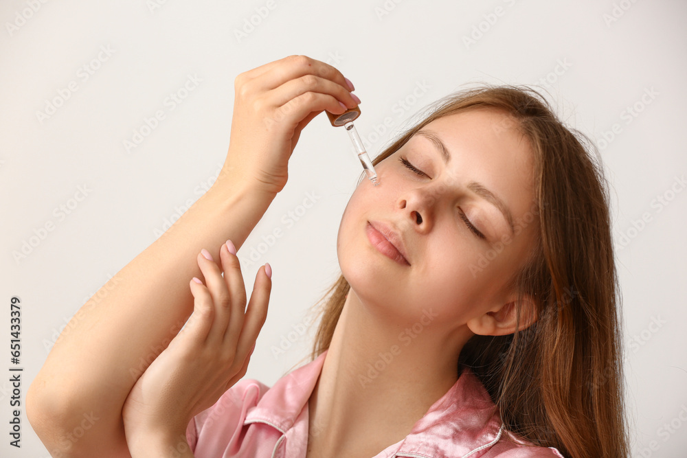 Pretty young woman with cosmetic oil on light background