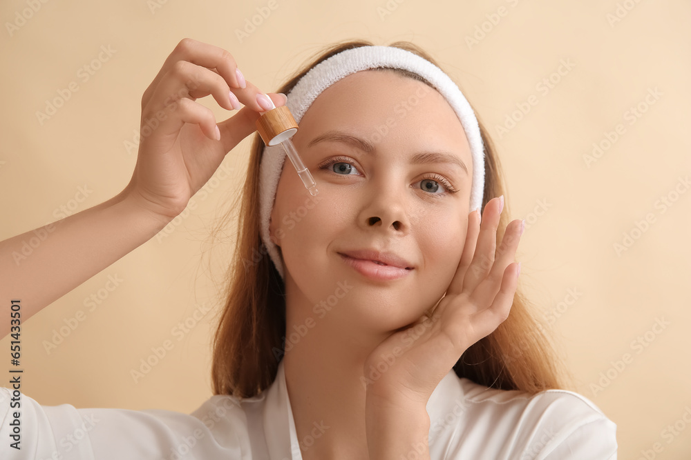 Pretty young woman with cosmetic oil on beige background